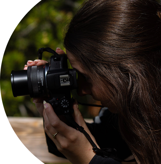 semicirclular image of the profile view of a woman pointing a camera to take a photo and looking through the viewfinder